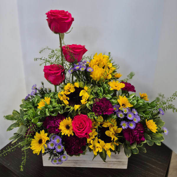Mixed floral arrangement with pink roses, yellow sunflowers, and purple daisies in a wooden box