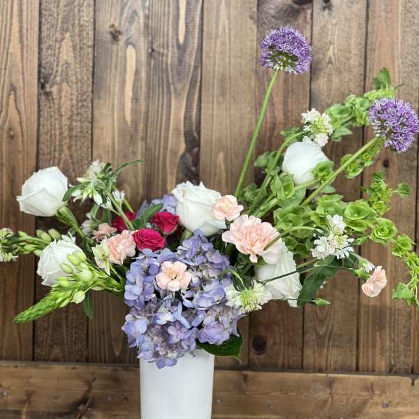 Mixed bouquet in a white vase with hydrangea, roses, and purple allium