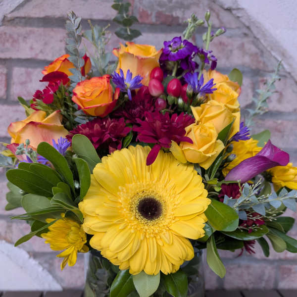 Colorful bouquet with yellow gerbera daisies and orange roses in a glass vase