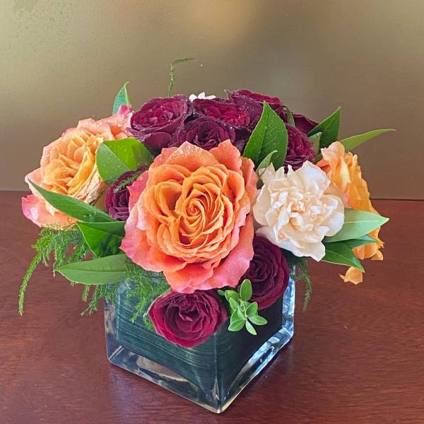 Bouquet of orange, burgundy, and white roses in a square glass vase