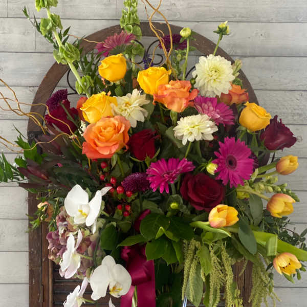 Mixed bouquet in a tall glass vase with roses, orchids, and bright daisies