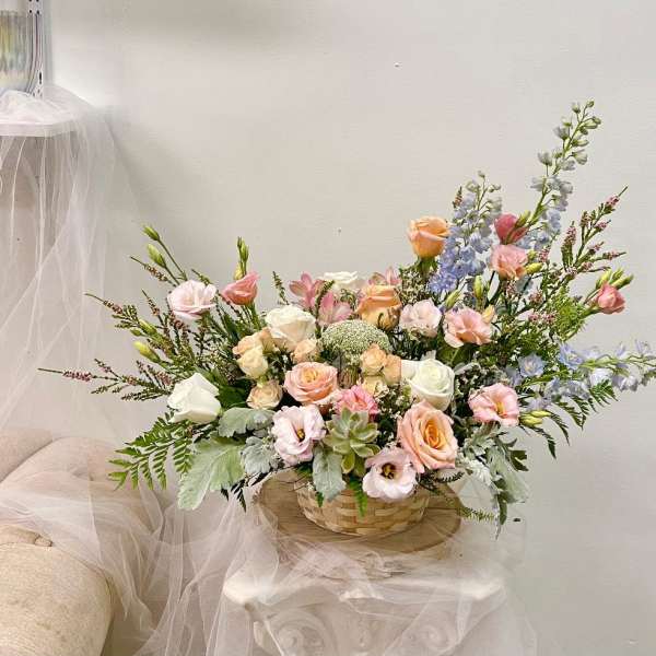 Pastel bouquet of roses, lisianthus, and blue delphinium in a woven basket