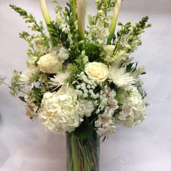 White floral arrangement in a clear glass vase with tall calla lilies and roses