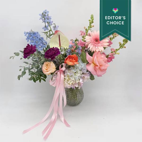 Mixed pastel flower arrangement in a glass vase with a pink ribbon