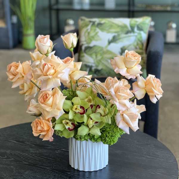 Peach roses and green orchids in a white vase