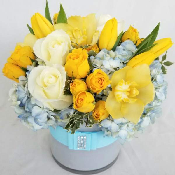 Yellow and white flower arrangement in a round hat box
