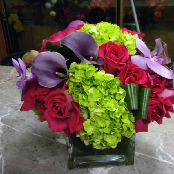 Bouquet of red roses, purple calla lilies, and green hydrangeas in a glass vase