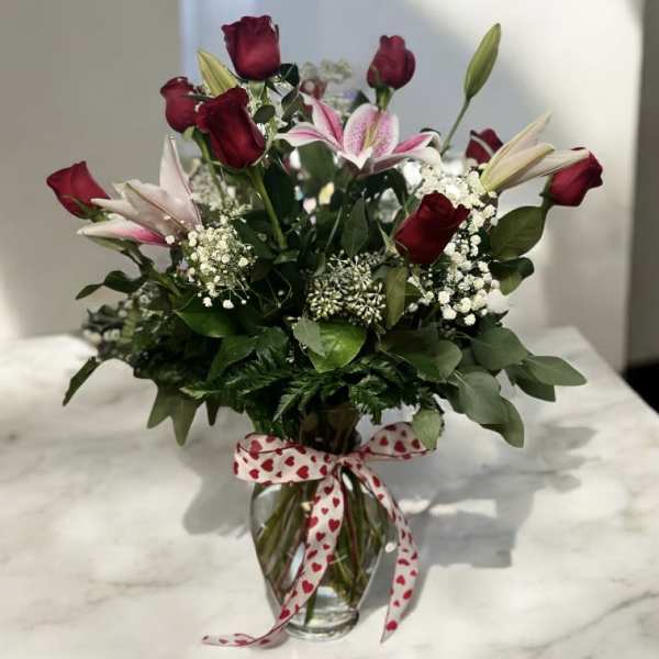 Bouquet of red roses and pink lilies in a glass vase with a heart ribbon