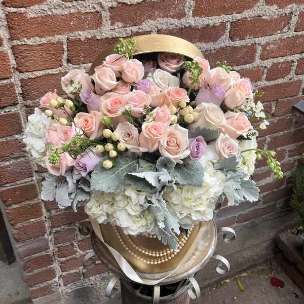 Pastel roses and hydrangeas arranged in a gold hatbox with ribbon