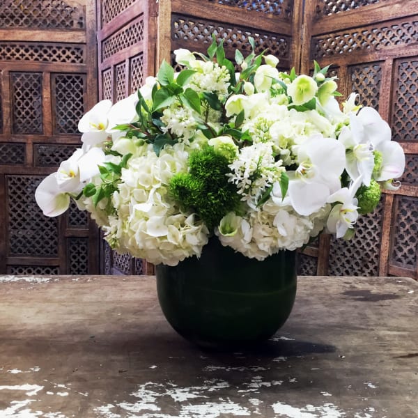 White floral arrangement in a dark vase with orchids and hydrangeas