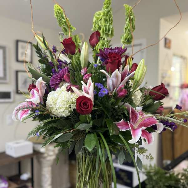 Tall mixed bouquet in a glass vase with red roses, lilies, and purple flowers