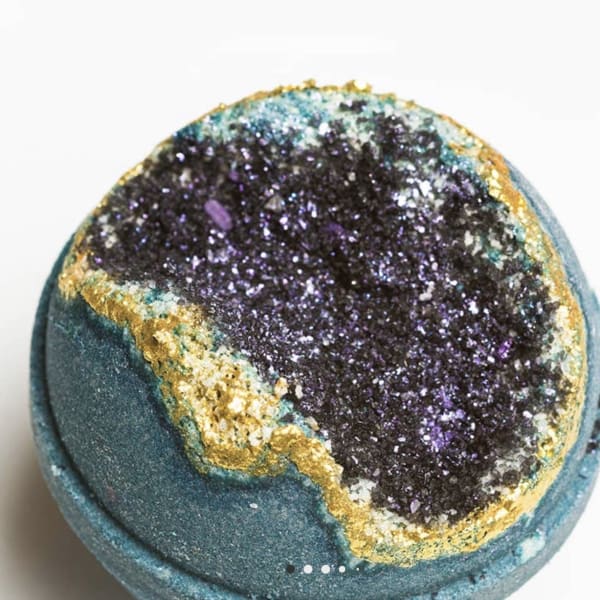 A teal bath bomb with a glittery purple and gold top
