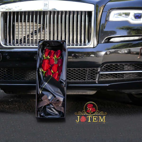Boxed bouquet of red roses in black wrapping in front of a car