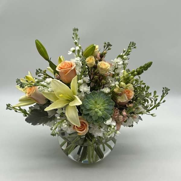 Peach roses and pale lilies in a round glass vase