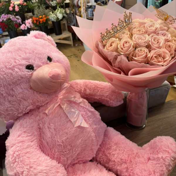 Pink teddy bear beside a bouquet of pale pink roses