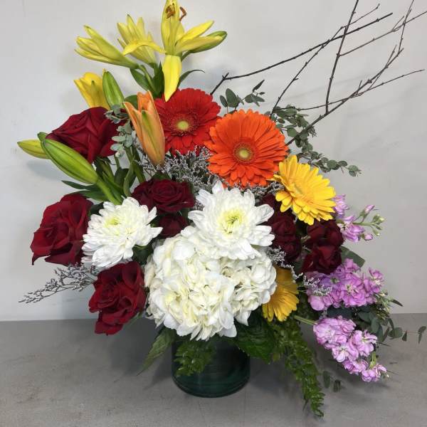 Colorful mixed bouquet with roses, lilies, gerberas, and white hydrangea in a glass vase