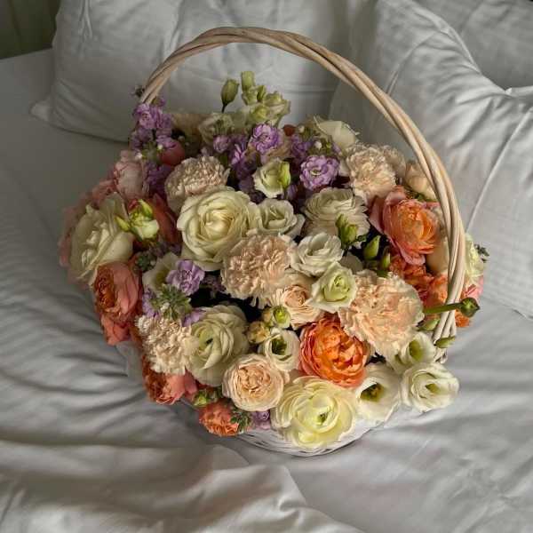 Basket of pastel roses, carnations, and purple blooms on white bedding