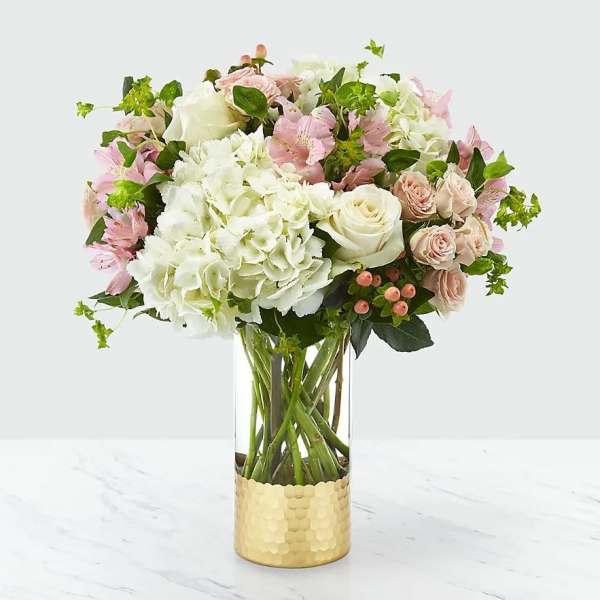 Pink and white flowers arranged in a clear glass vase with a gold base