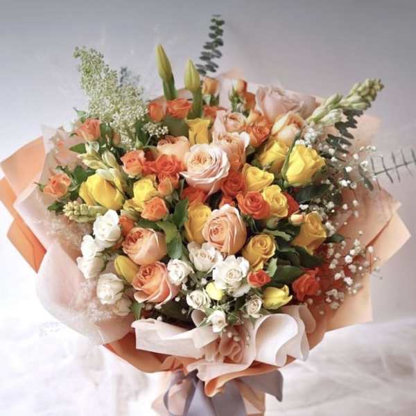 Bouquet of peach, yellow, and white roses wrapped in pastel paper