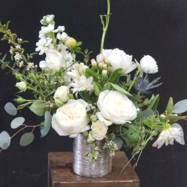 White floral arrangement in a silver vase on a wooden stand