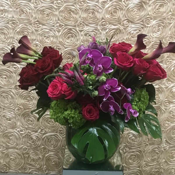 Bouquet of red roses, purple orchids, and calla lilies in a green vase