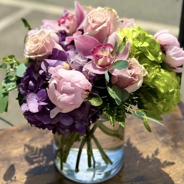 Pink roses and orchids arranged with purple hydrangeas in a glass vase