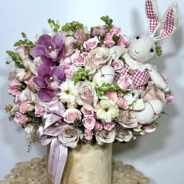 Pink and white floral arrangement with plush bunny figures in a vase
