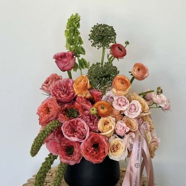 Mixed bouquet of pink, peach, and orange flowers in a black vase