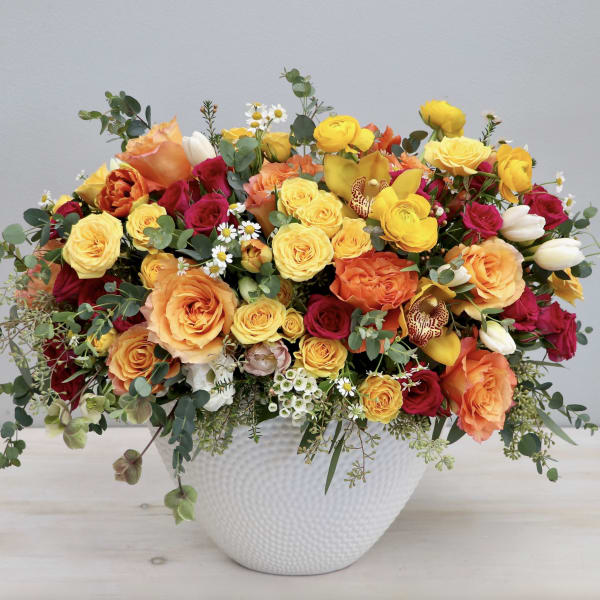 Mixed bouquet of yellow, orange, and red flowers in a white vase