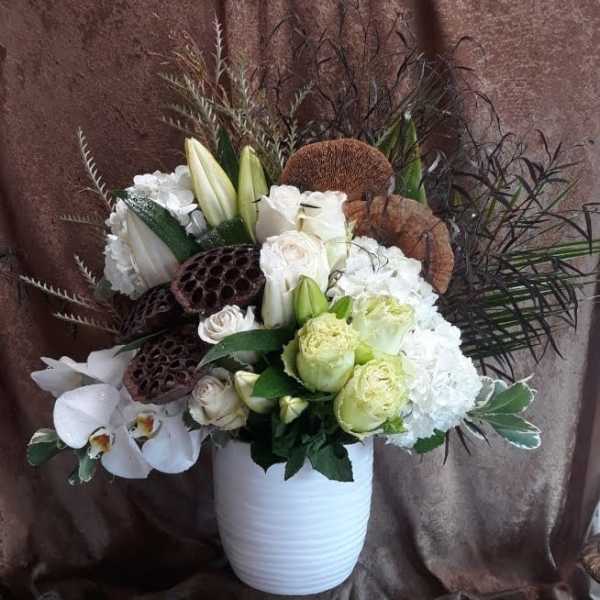 White floral arrangement in a white vase with orchids and lilies