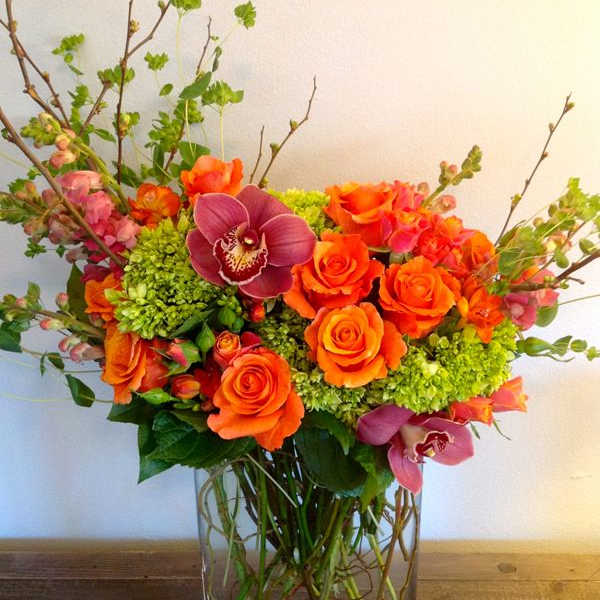 Orange roses and magenta orchids in a clear glass vase