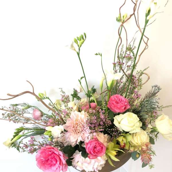 Pink and cream floral arrangement with tall branches in a low container