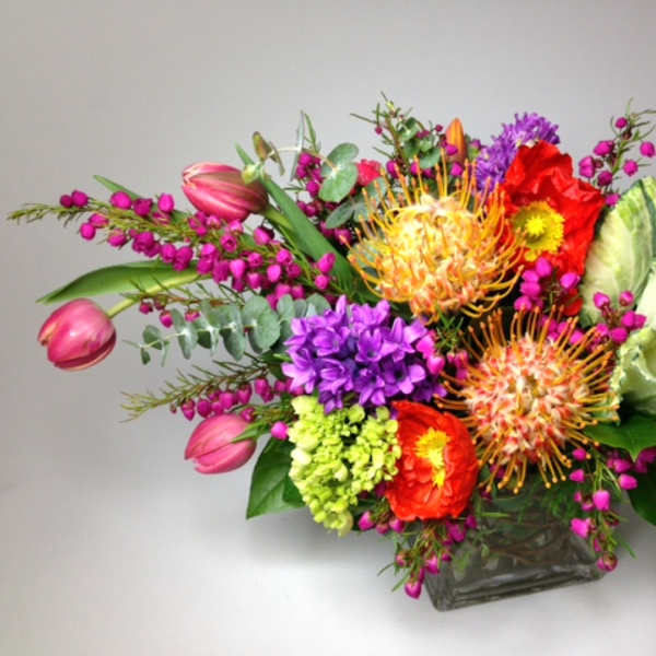 Colorful mixed bouquet in a square glass vase with pink tulips and purple blooms