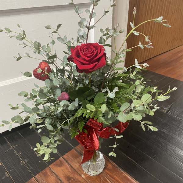 Single red rose arrangement in a small clear vase with a red ribbon