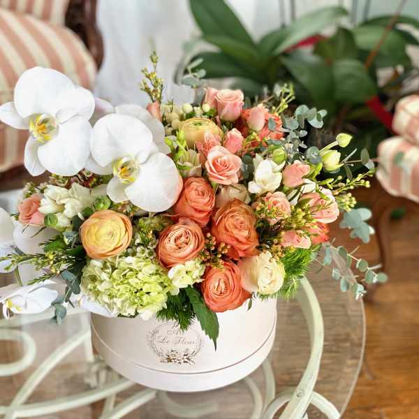 Peach roses and white orchids arranged in a round white box