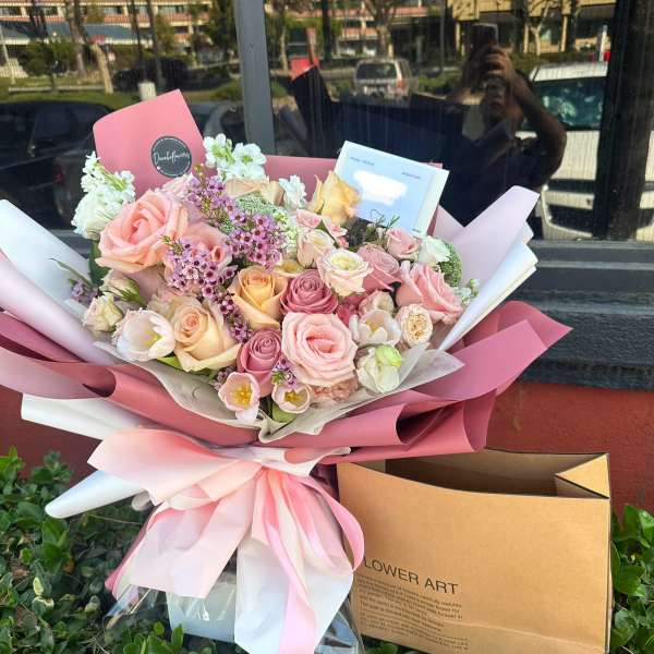 Pink and cream rose bouquet wrapped in pink paper with a ribbon