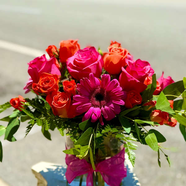 Pink and orange roses with a magenta daisy in a glass vase