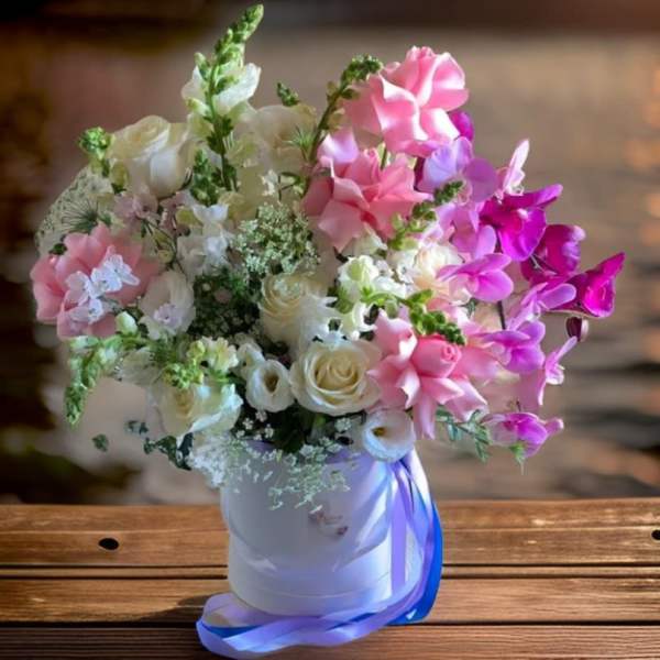 Pink and white floral arrangement in a white hatbox with blue ribbon