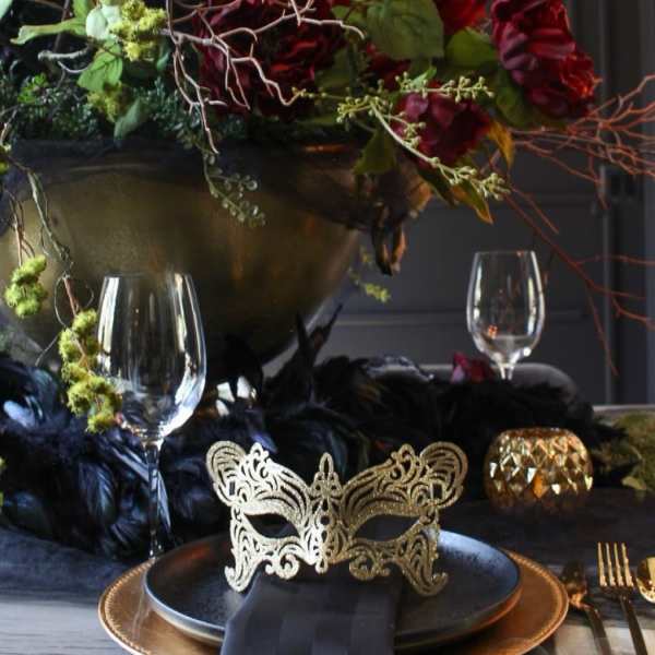 Dark floral centerpiece with red blooms in a gold bowl on a decorated table