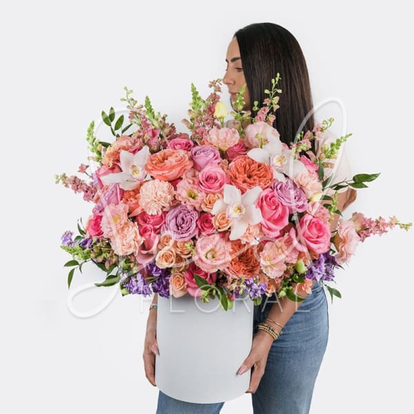 Large pink and peach flower arrangement in a white box held by a woman