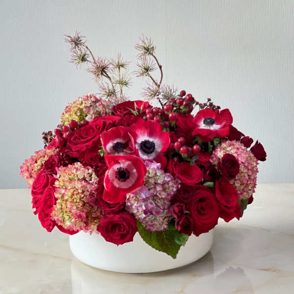 Red roses and anemones arranged in a white bowl vase