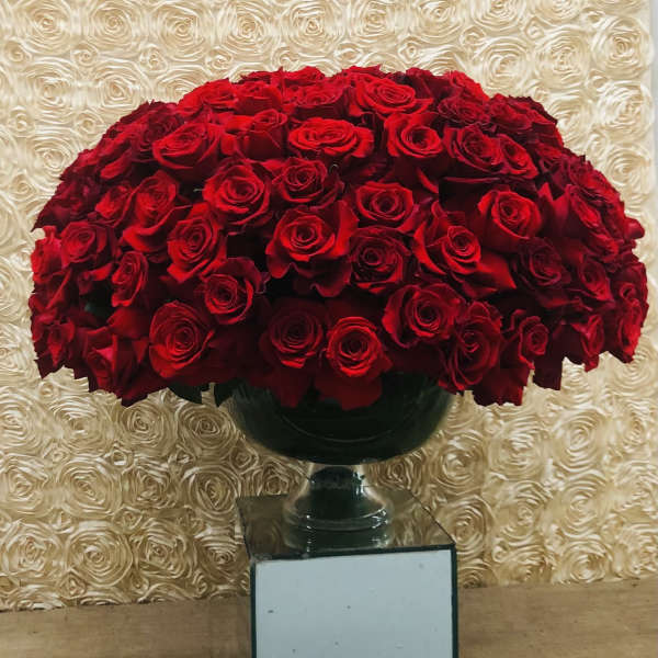 Large bouquet of red roses in a dark vase on a mirrored pedestal