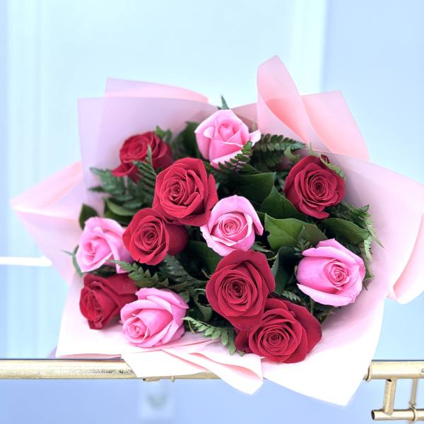 Hand-tied bouquet of red and pink roses wrapped in soft pink paper