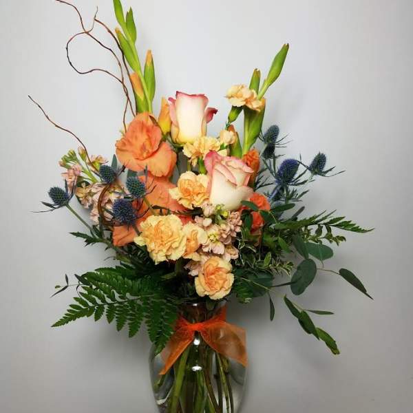 Orange and cream floral arrangement in a glass vase with a ribbon