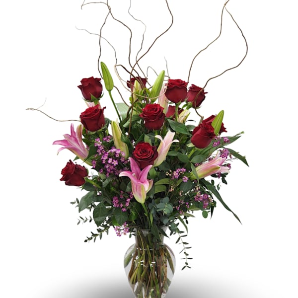 Red roses and pink lilies in a clear glass vase with curly branches