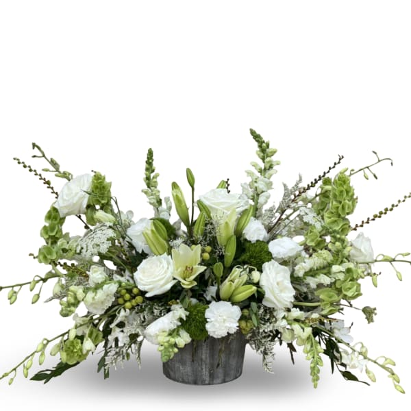 Low white and green arrangement with roses, lilies, and snapdragons in a rustic gray container