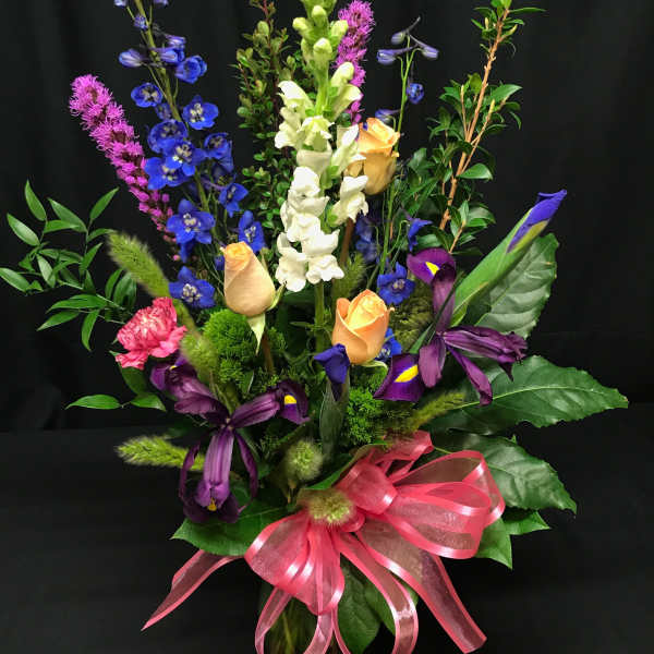 Tall mixed bouquet with blue, white, purple, and peach flowers in a glass vase