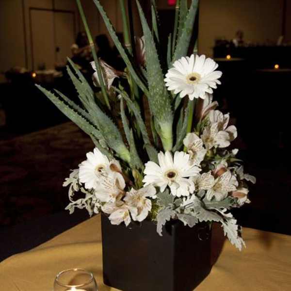 White gerbera daisies and pale flowers in a black vase with tall spiky foliage
