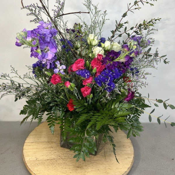 Tall mixed bouquet with purple, pink, and white flowers in a glass vase