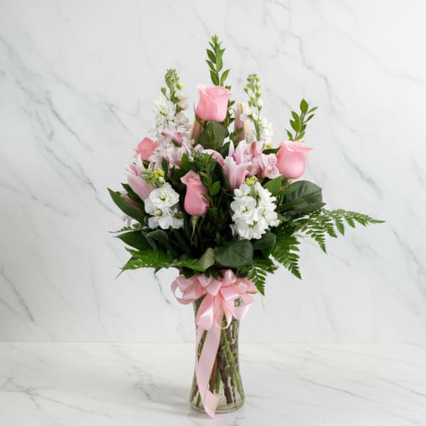 Pink roses and white flowers arranged in a glass vase with a pink ribbon